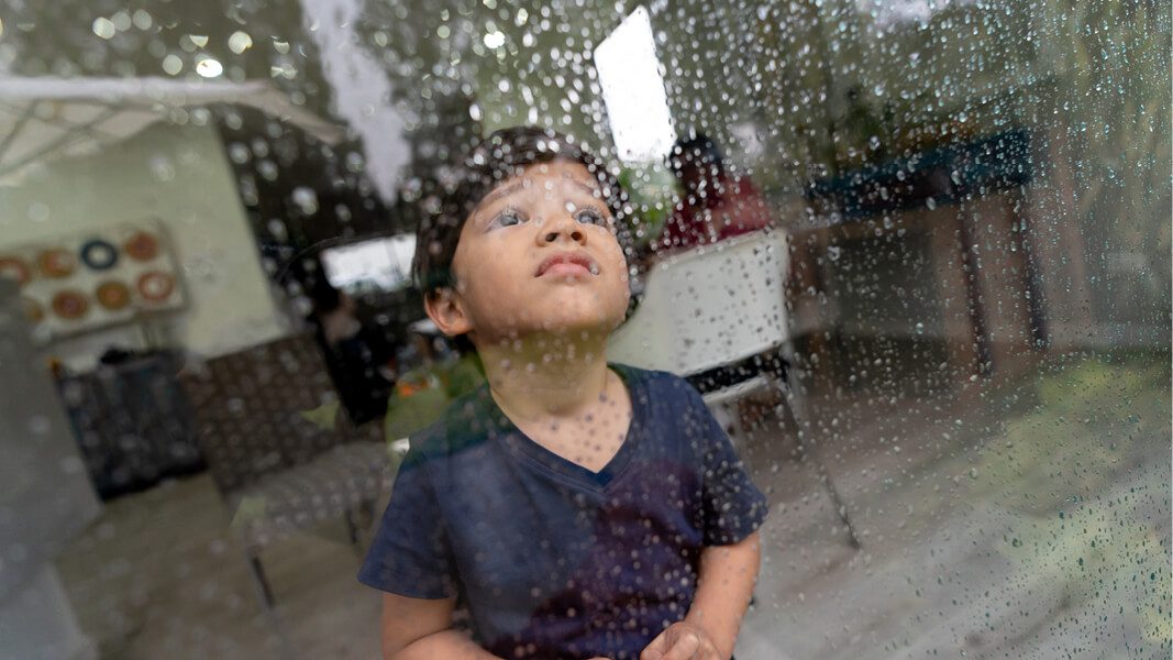 Young boy looking out rainy window